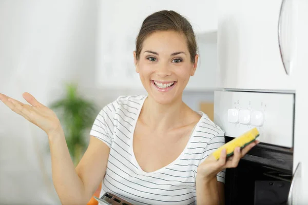 Positiva giovane casalinga bionda che fa pulizia del forno in cucina domestica — Foto Stock