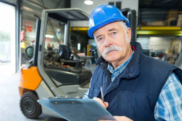 Trabajador senior con un portapapeles trabajando en una carretilla elevadora — Foto de Stock