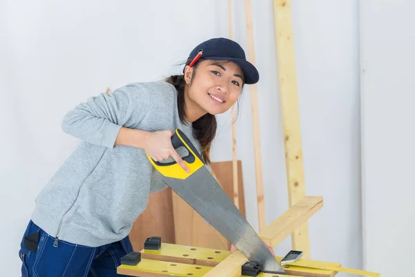 Young female carpenter cutting timber using manual saw — Stock Photo, Image
