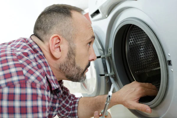 Man op zoek naar wasmachine trommel terwijl het houden van tangen — Stockfoto