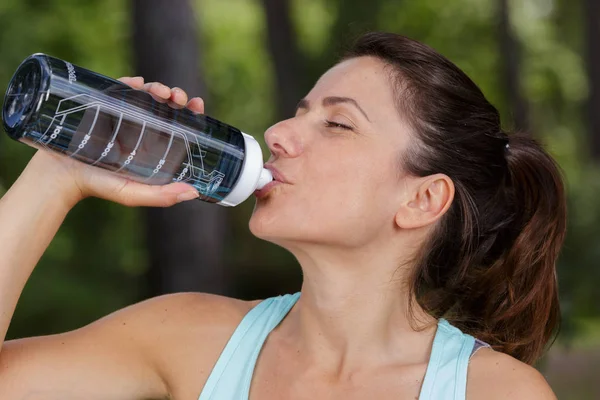 Woman drinking water on park bench — Stock Photo, Image