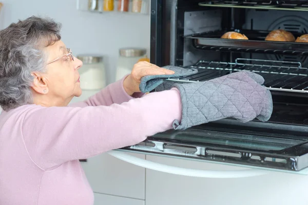 Mulher idosa removendo bandeja do forno — Fotografia de Stock