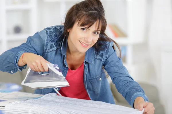 Woman standing next to an ironing board — Stock Photo, Image