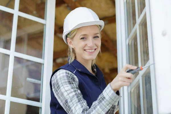 Kobieta ubrana w hardhat mocowania okna — Zdjęcie stockowe