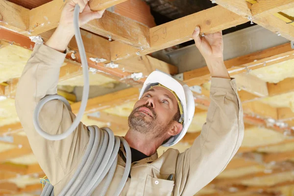 Будівельник годує стовбур кабелю в деревину даху — стокове фото