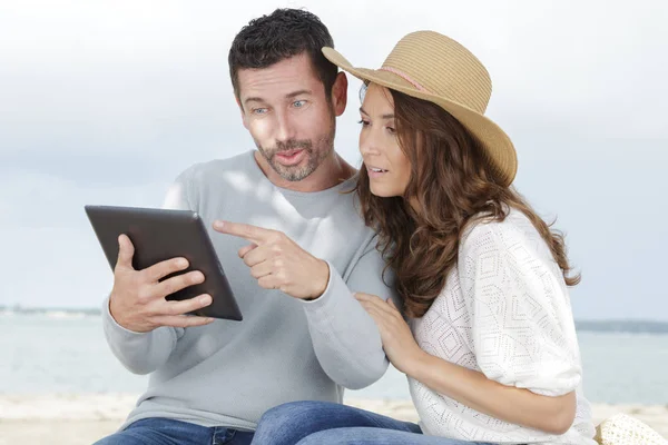 Casal amoroso usando um tablet na praia — Fotografia de Stock