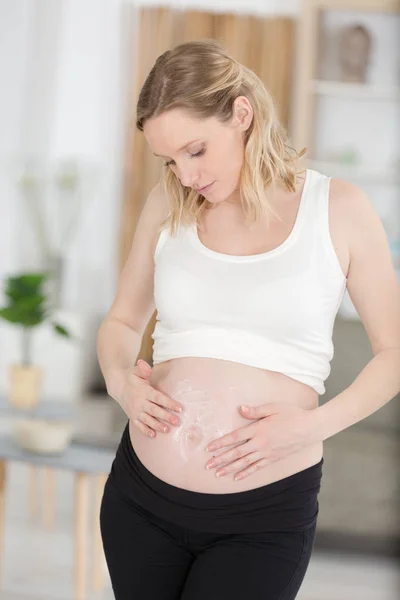 Donna incinta che applica la crema alla pancia — Foto Stock