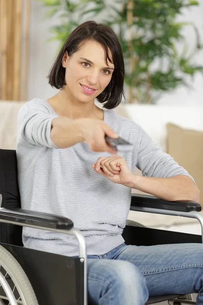 Femelle en fauteuil roulant tenant une télécommande TV — Photo