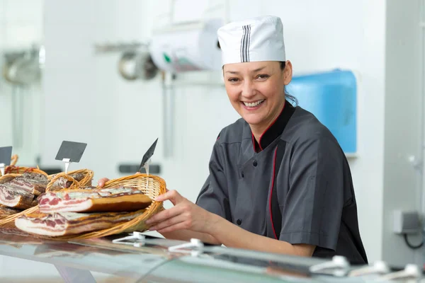 Szczęśliwa kobieta sprzedaje pyszne mięso prosciutto na rynku — Zdjęcie stockowe