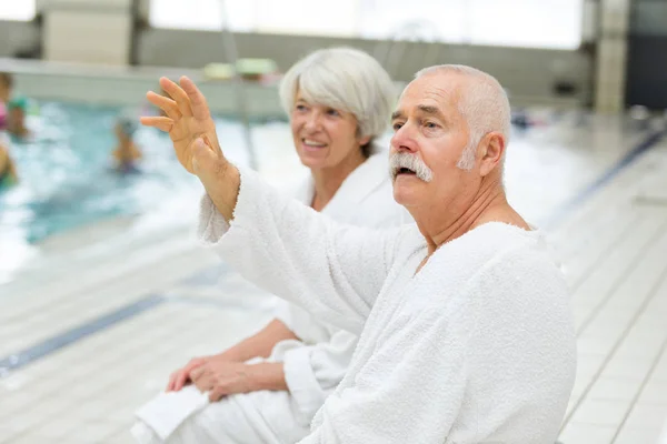 Seniorer bär en badrock som står bredvid en pool — Stockfoto