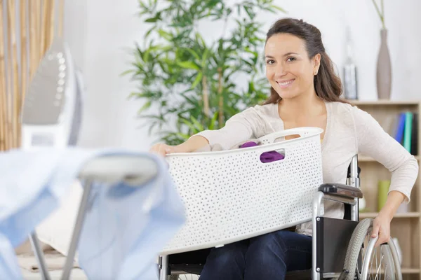 Mujer feliz en silla de ruedas llevando cesta de lavandería — Foto de Stock