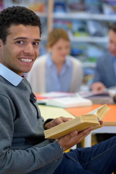 Fiatal mosolygós férfi könyvet olvasott a könyvtárban — Stock Fotó