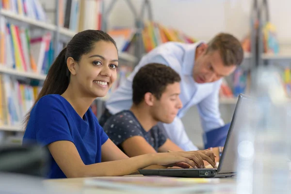 Giovani studenti che fanno i compiti con il computer portatile in biblioteca — Foto Stock