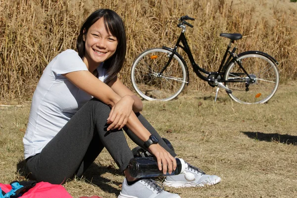 Mooie jonge vrouw zittend op gras naast de fiets — Stockfoto