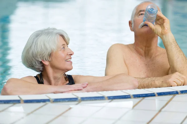 Casal idoso beber água engarrafada enquanto na piscina spa — Fotografia de Stock