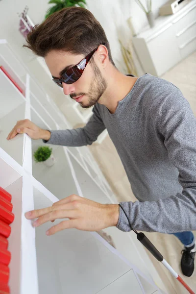 Blind man letar efter något på en hylla hemma — Stockfoto
