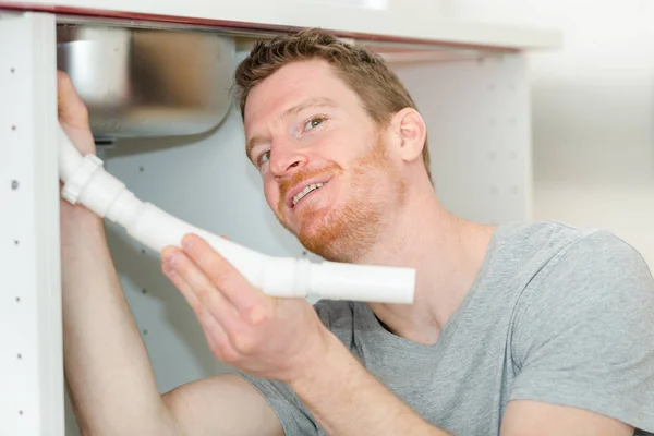 portrait of man fitting waste pipe under sink