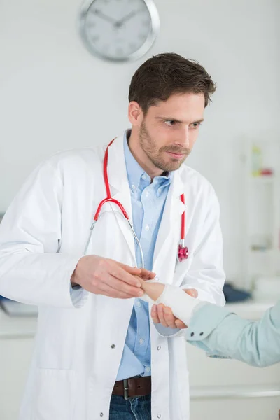 Ein erwachsener Arzt, der seine Patientin im Krankenhaus bandagiert — Stockfoto