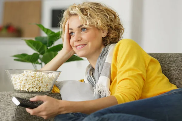 Kobieta układanie na kanapie trzymając popcorn — Zdjęcie stockowe