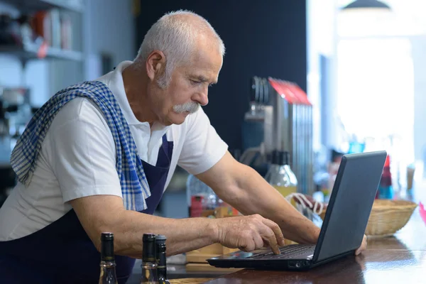 Homem sênior barista usando laptop — Fotografia de Stock