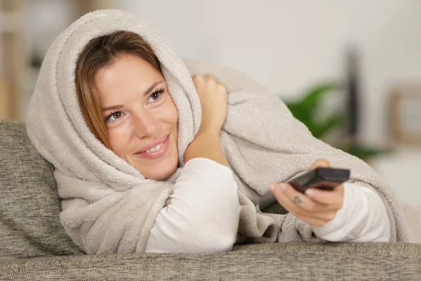 Mujer envuelta en manta usando control remoto — Foto de Stock