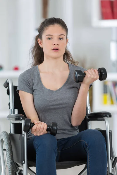 Tekerlekli sandalyeye mahkum dumbbells yükselen genç kız — Stok fotoğraf