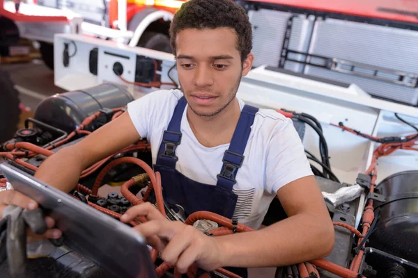 Endüstriyel araç üzerinde çalışırken tablet kullanarak genç erkek mekanik — Stok fotoğraf
