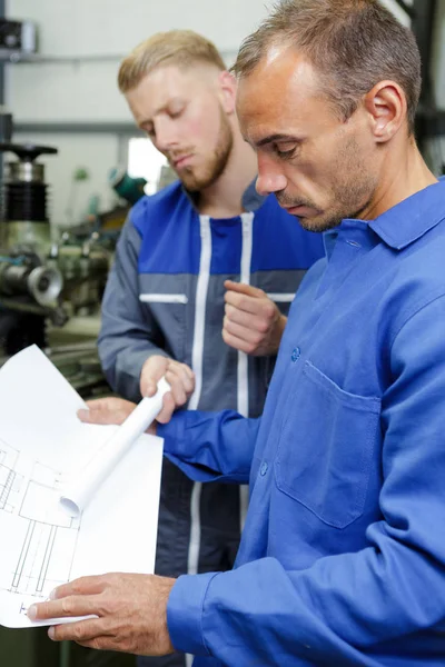 Männer in Fabrik schauen sich Papiere an — Stockfoto