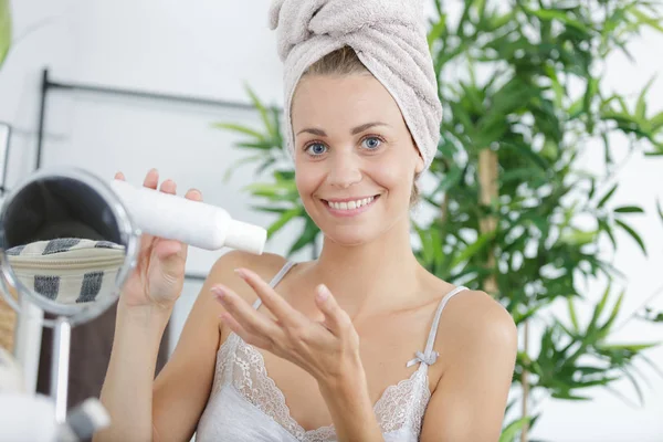 Woman sat at mirror applying skincare product — Stock Photo, Image