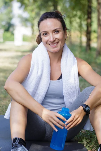 Frau hält Wasserflasche mit Handtuch auf Schultern — Stockfoto