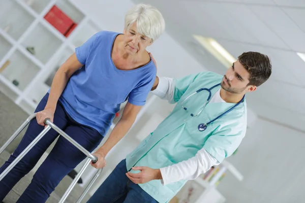 Verpleegkundige helpen senior vrouw gebruikt een wandelende frame — Stockfoto