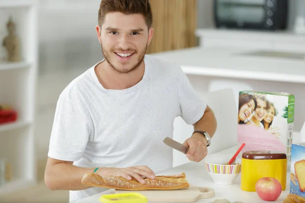 Retrato de un joven cortando baguette para el desayuno — Foto de Stock