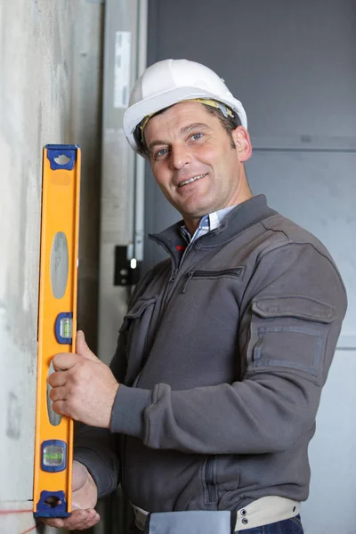 Engineer in helmet is measuring wall with level — Stock Photo, Image