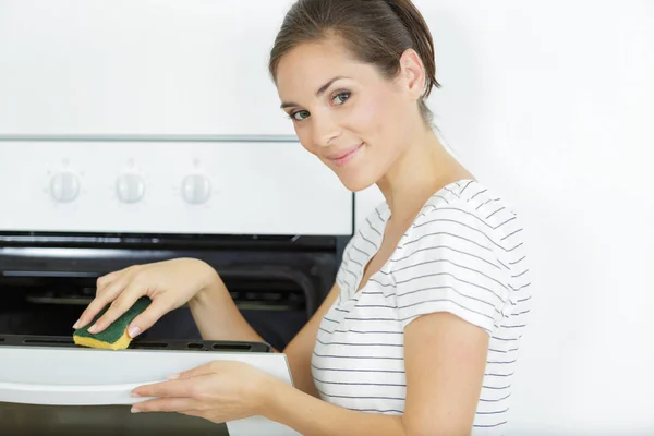 Portret van jonge vrouw schoonmaak oven in huis — Stockfoto