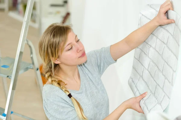 Femme déroulant rouleau de papier peint contre le mur — Photo