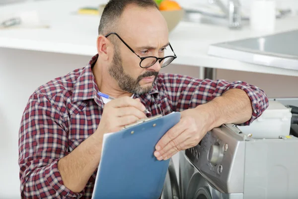 Máquina de lavar roupa serviceman olhando por cima de óculos para escrever — Fotografia de Stock