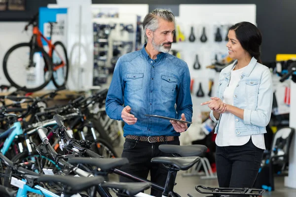 Sprzedawca i kobieta klient patrząc na rowery — Zdjęcie stockowe