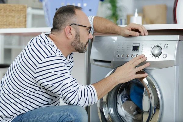 Hombre cargando ropa en la lavadora en la cocina —  Fotos de Stock