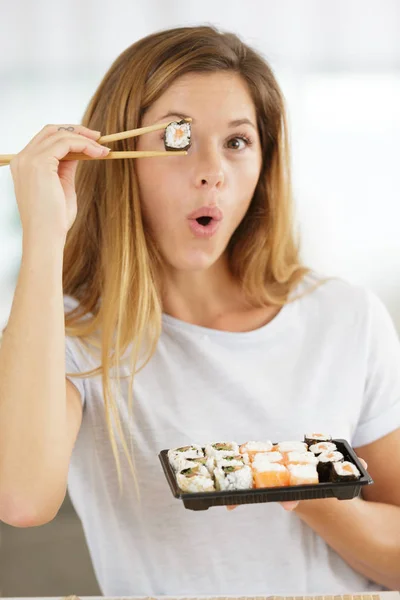 Femme souriante tenant des sushis devant les yeux avec des baguettes — Photo