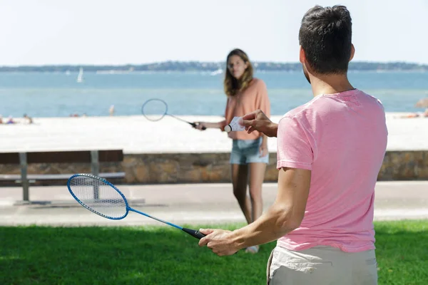 Jeune couple souriant jouant au badminton en plein air — Photo