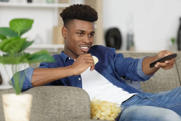 Homem come enquanto detém tv controle remoto — Fotografia de Stock