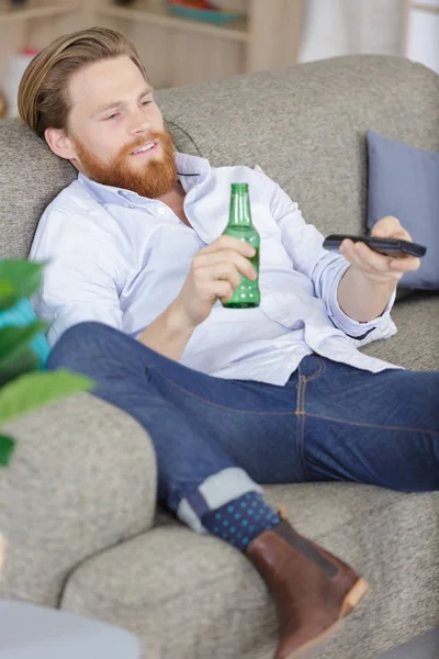Άνθρωπος κρατώντας ένα άδειο μπουκάλι μπύρας ενώ βλέποντας τηλεόραση — Φωτογραφία Αρχείου