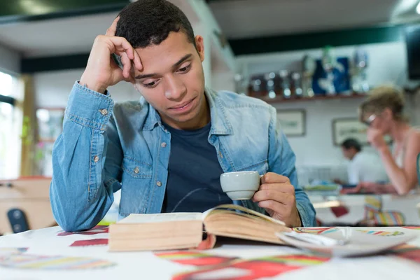Junger Mann allein am Cafétisch beim Lesen von Buch — Stockfoto
