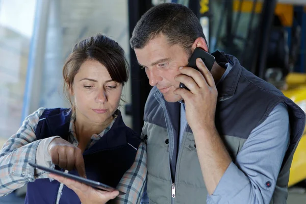 Trabajadores de almacén mirando la tableta y el uso de teléfonos inteligentes — Foto de Stock