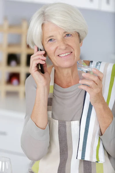 Senior woman holding a phone call while drinking water — Stock Photo, Image