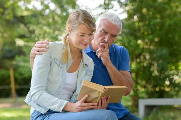 Vrouw en grootvader op een bankje tijdens het lezen van een boek — Stockfoto