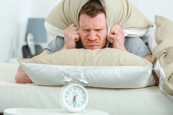 Angry man lying in the bed with pillow on head — Stock Photo, Image