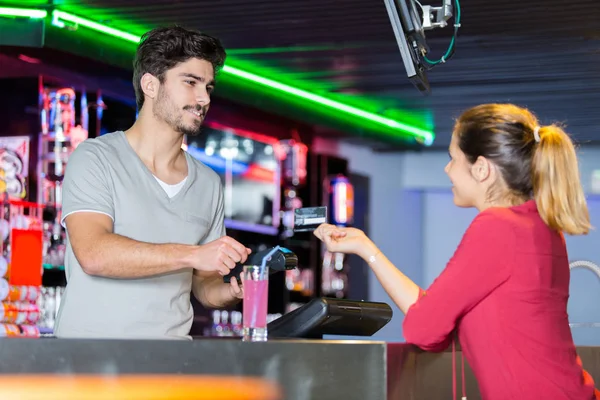 Young attractive waiter giving a drink to female customer — Stockfoto