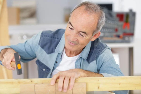 Uomo anziano martellante tasselli di legno a casa — Foto Stock