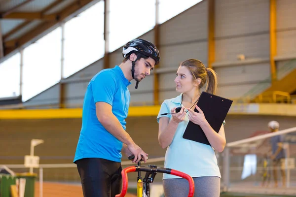 Mujer entrenadora hablando con un hombre haciendo bicicleta estática —  Fotos de Stock